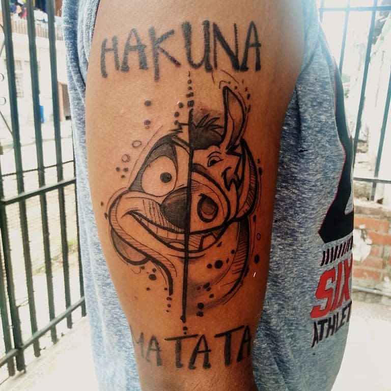Timon and Pumbaa arm tattoo with 'Hakuna Matata' text, symbolizing carefree living